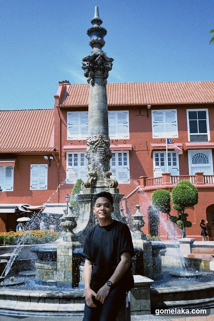 Person in front of fountain and red building