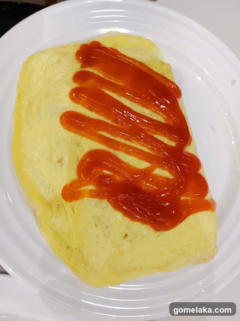 A yellow omelette on a white plate, topped with zigzagged ketchup drizzle.