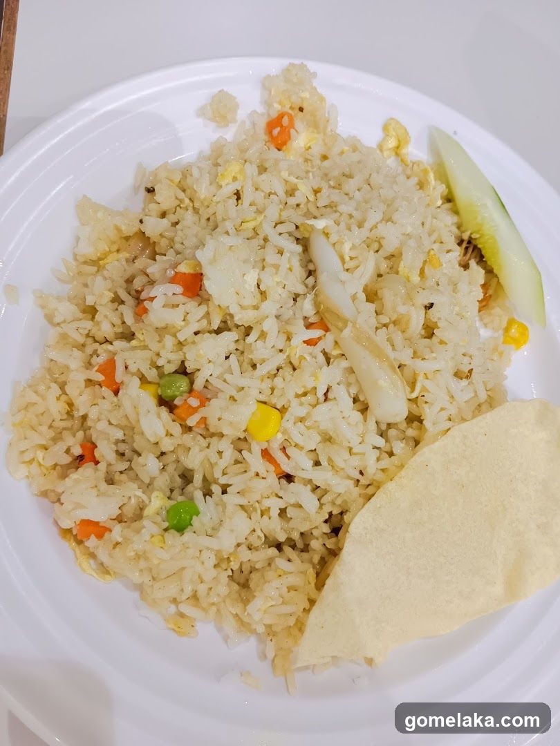 A plate of fried rice with vegetables, egg, and a side of cucumber slice and crispy flatbread.