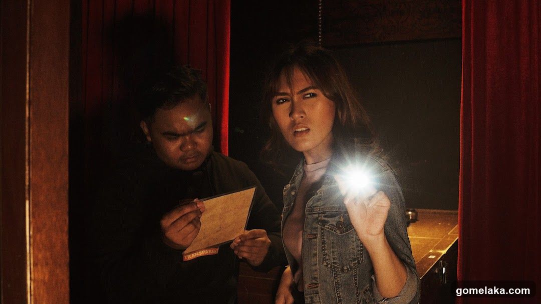 Two people in dimly lit room with red curtains