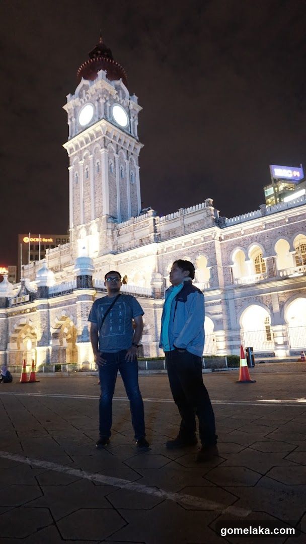 Two individuals standing in front of a lit historical building at night