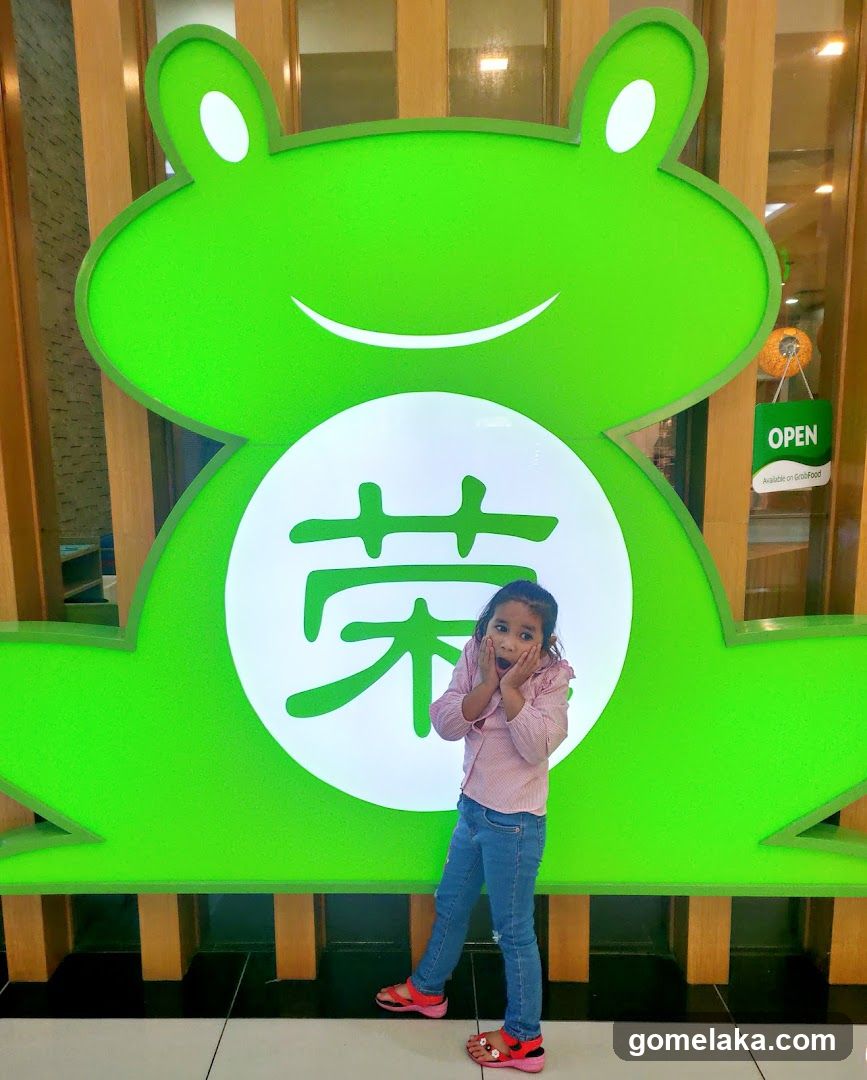 Child posing in front of green frog-shaped sign