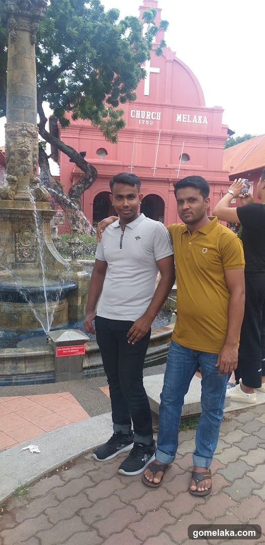 Two men posing in front of a fountain and red church