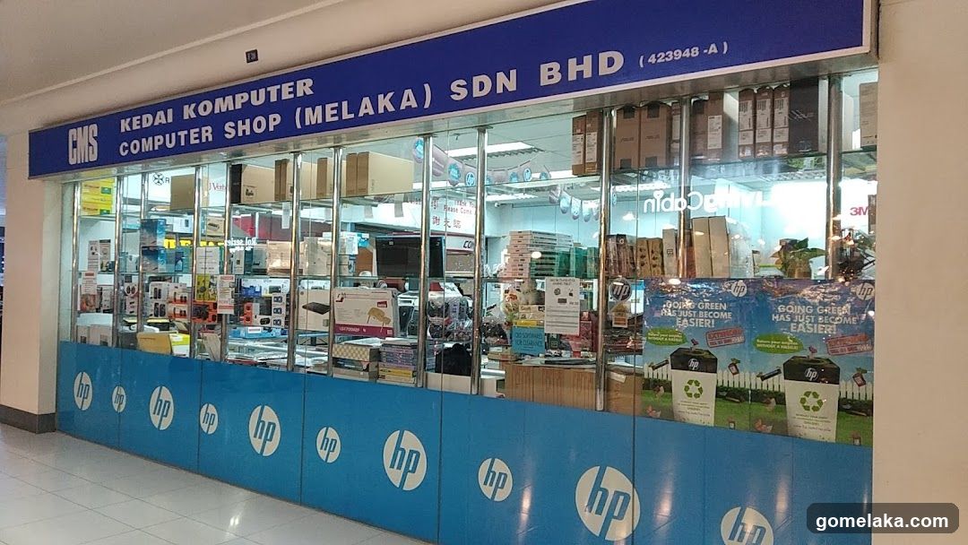 Storefront with blue signage displaying business name and registration number (423948-A). Glass windows show interior shelves stocked with computer parts and accessories. Blue HP logo panels line the bottom of the facade.