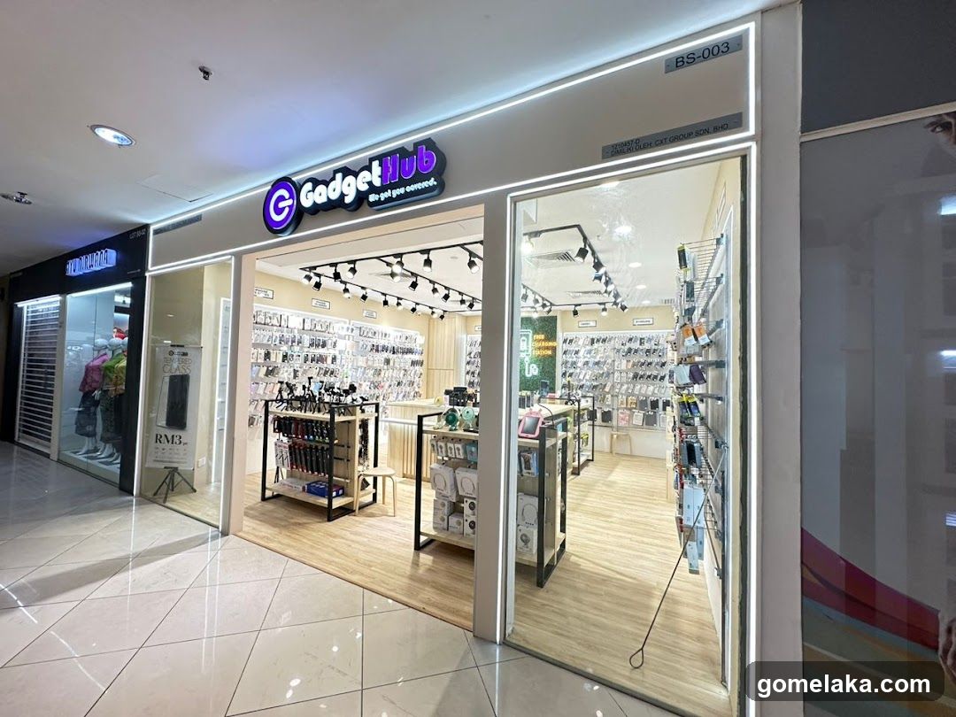 Store entrance with illuminated 'GadgetHub' sign, glass doors and windows, wooden flooring inside, visible racks of gadgets. Signage includes 'BS-003' and 'JALAN BUKIT GADGET GROUP SDN.BHD.'