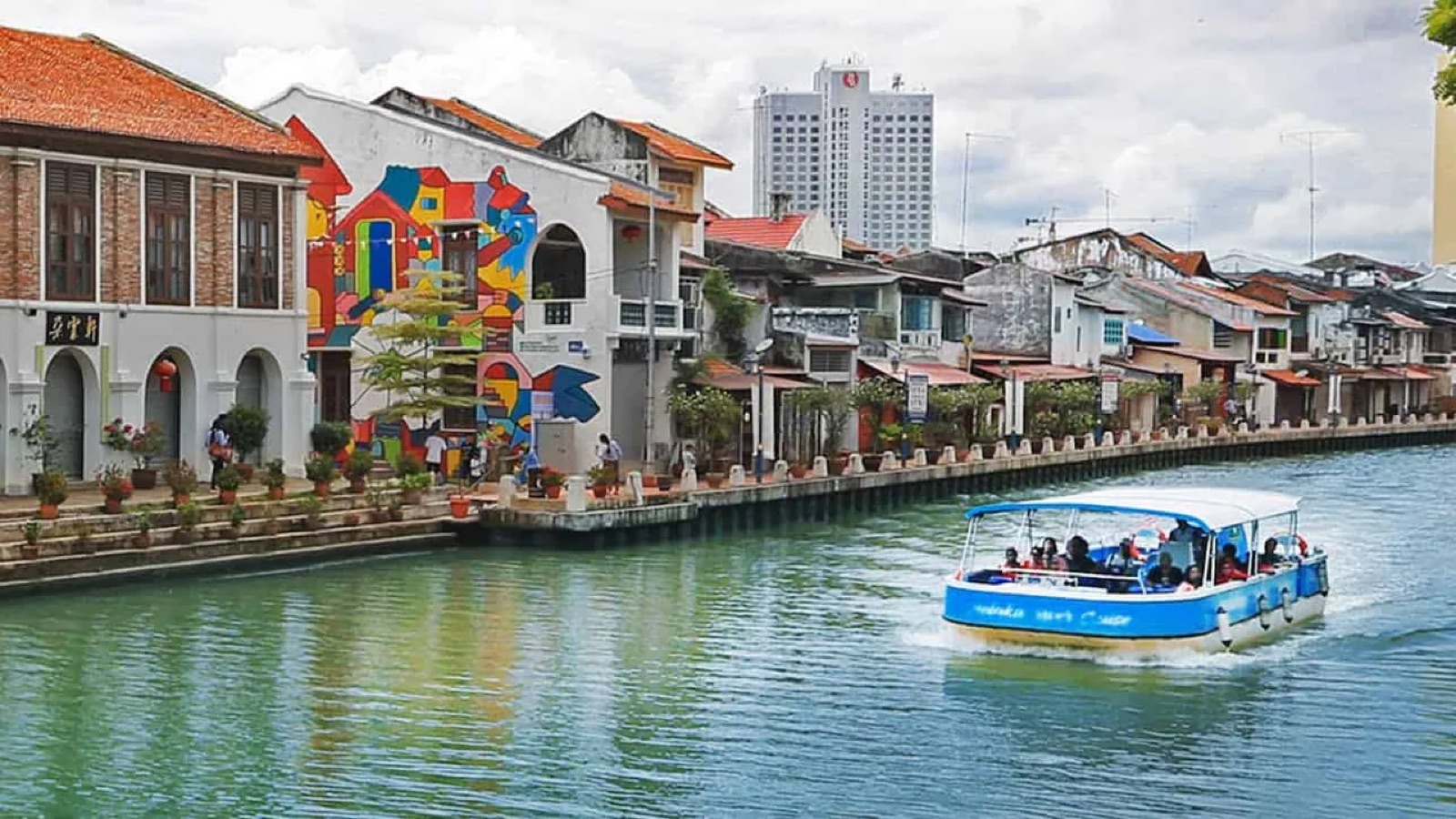 Daytime Melaka River Cruise boat passing riverside murals in Bandar Hilir